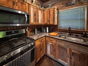A kitchen with wooden cabinets, a stainless steel microwave, a stove, and a window with blinds. - *NEW* River Valley Retreat ~ directly on White River (Mountain View)