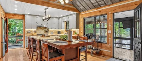 A spacious kitchen with wooden beams, a large island with bar stools, and a view through the glass doors.