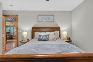 A bedroom with a wooden headboard, a bed with striped bedding, two bedside lamps, and a wall sign.