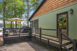 Eine Holzjagdhuette mit grüner Fassade, eine überdachte Veranda mit Gartenmöbeln und Blick auf die umliegenden Bäume.