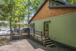 A cabin with a deck overlooking a lake, featuring outdoor seating and a staircase.