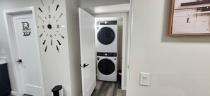 A laundry room with a wall-mounted clock and stacked washing machines. - Daisy's Inn (Saskatoon)