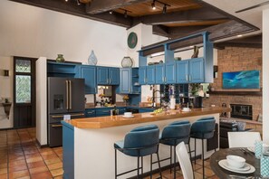 Une cuisine moderne avec des meubles bleus, un îlot central doté de tabourets de bar, un réfrigérateur noir et un mur en briques avec une cheminée.