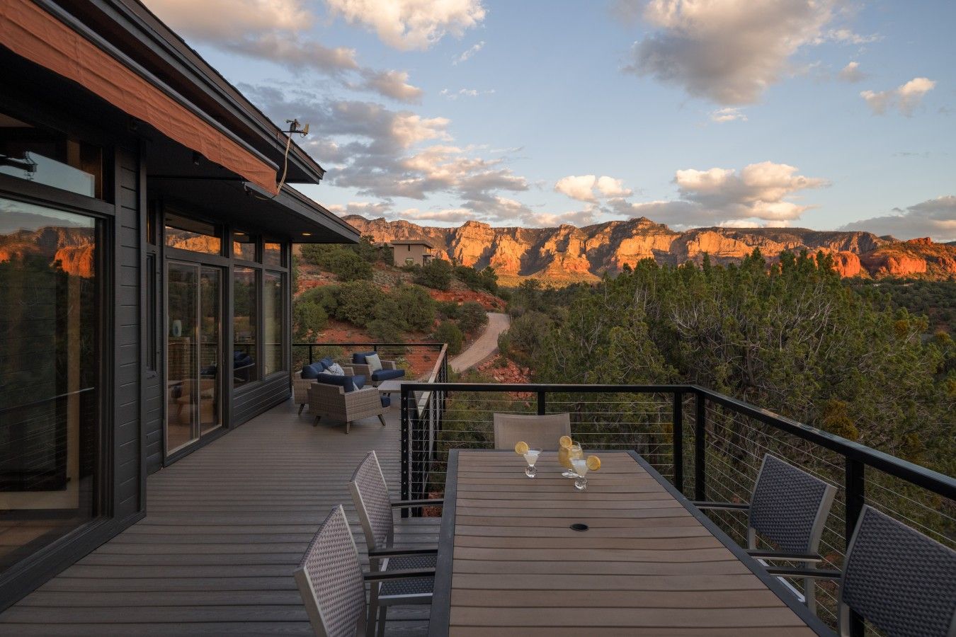 A modern outdoor deck with a table and chairs, overlooking a canyon with a winding road.