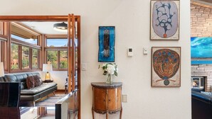 A room with a sofa, a small table with a vase, and artwork on the wall. - Palisades Villa | 360 Views, Hot Tub, Mid-Century (Sedona)