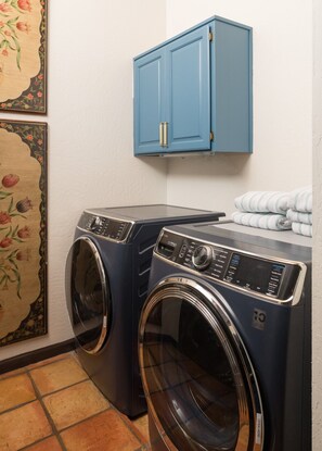 A laundry area with two front-loading washing machines, a blue cabinet above, and a tiled floor. - Palisades Villa | 360 Views, Hot Tub, Mid-Century (Sedona)