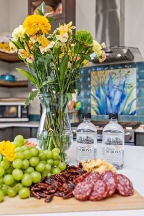 A table with a vase of flowers, bottles of water, grapes, pecans, and sliced salami. - Rancho Rojo | Red Rock Views, Hot Tub, Private (Sedona)