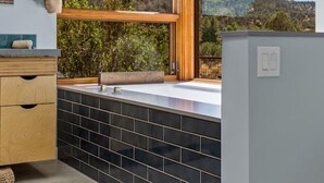 A modern bathroom with a large window, a wooden vanity, a mirror, and a sink. - Rancho Rojo | Red Rock Views, Hot Tub, Private (Sedona)
