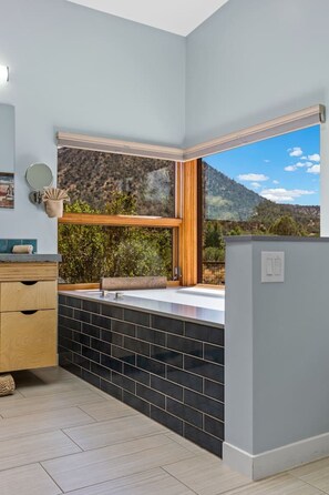 Ein modernes Badezimmer mit großem Fenster, einem Holzwaschtisch, einem Spiegel und einem Waschbecken.
