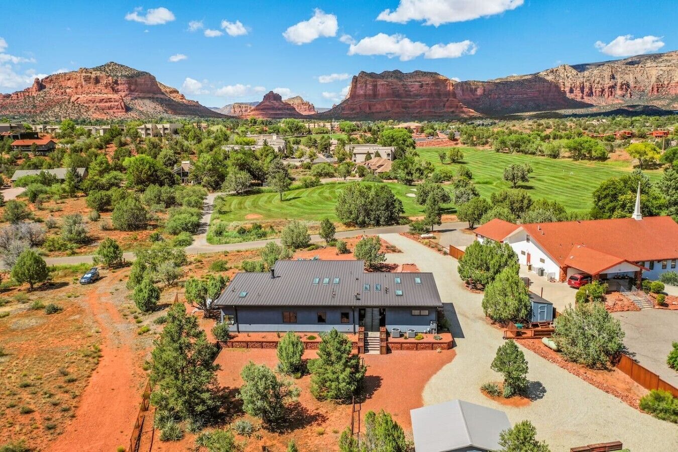 A residential area with houses, a golf course, and red rock formations in the background.