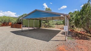 A covered outdoor area with a gravel floor, a metal roof, and a sign indicating guest parking. - Rancho Rojo | Red Rock Views, Hot Tub, Private (Sedona)
