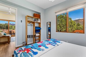 A bedroom with a bed, a wooden wardrobe, a window with a view, and a door leading to a balcony. - Rancho Rojo | Red Rock Views, Hot Tub, Private (Sedona)
