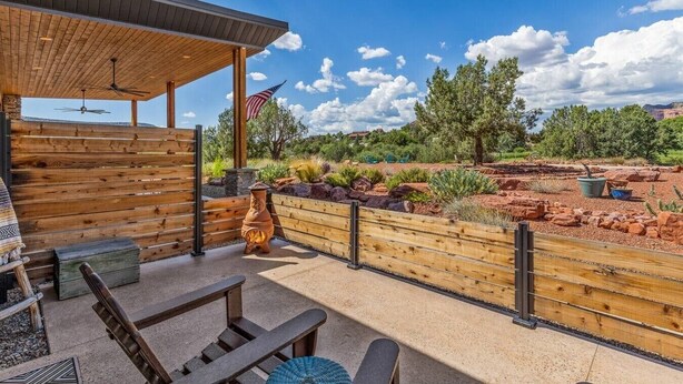 An outdoor patio with a wooden fence, a flag, and a view of a natural landscape. - Rancho Rojo | Red Rock Views, Hot Tub, Private (Sedona)