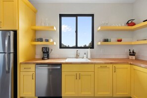 Eine Küche mit gelben Schränken, einem Edelstahl-Kühlschrank, einem Geschirrspüler, einer Kaffeemaschine und einem Fenster mit Blick.