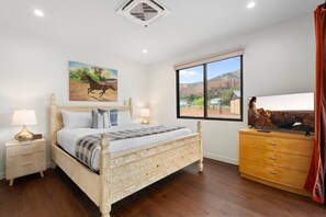 Ein Schlafzimmer mit einem großen Bett, einem Fernseher, einem Schminktisch und einem Fenster mit Blick auf eine Wüstenlandschaft.