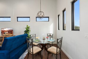 Ein Essbereich mit einem runden Glastisch, vier Stühlen, einem blauen Sofa und einer Chandelüster.