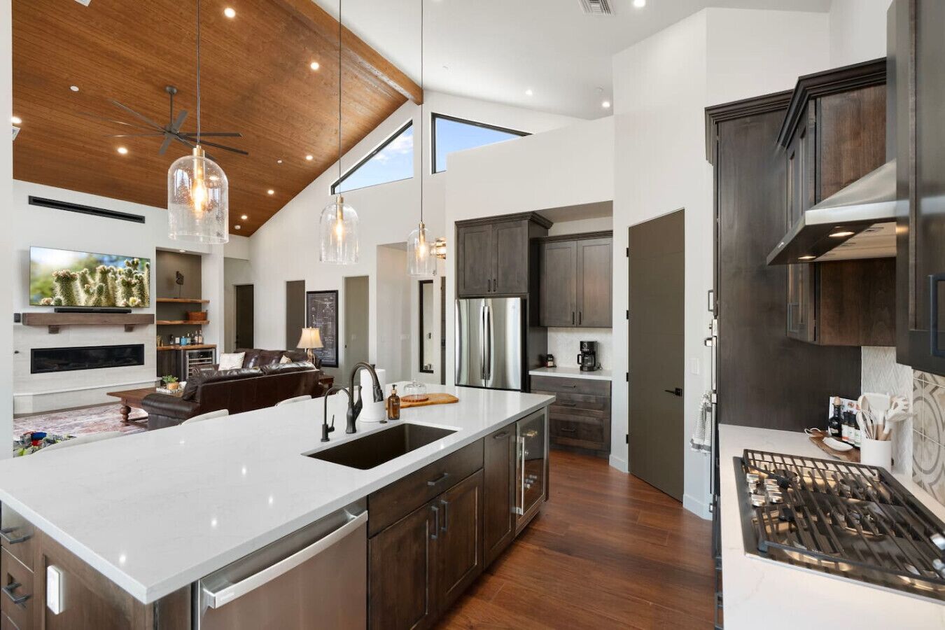 A modern kitchen with a large island, dark wood cabinets, stainless steel appliances, and pendant lighting.