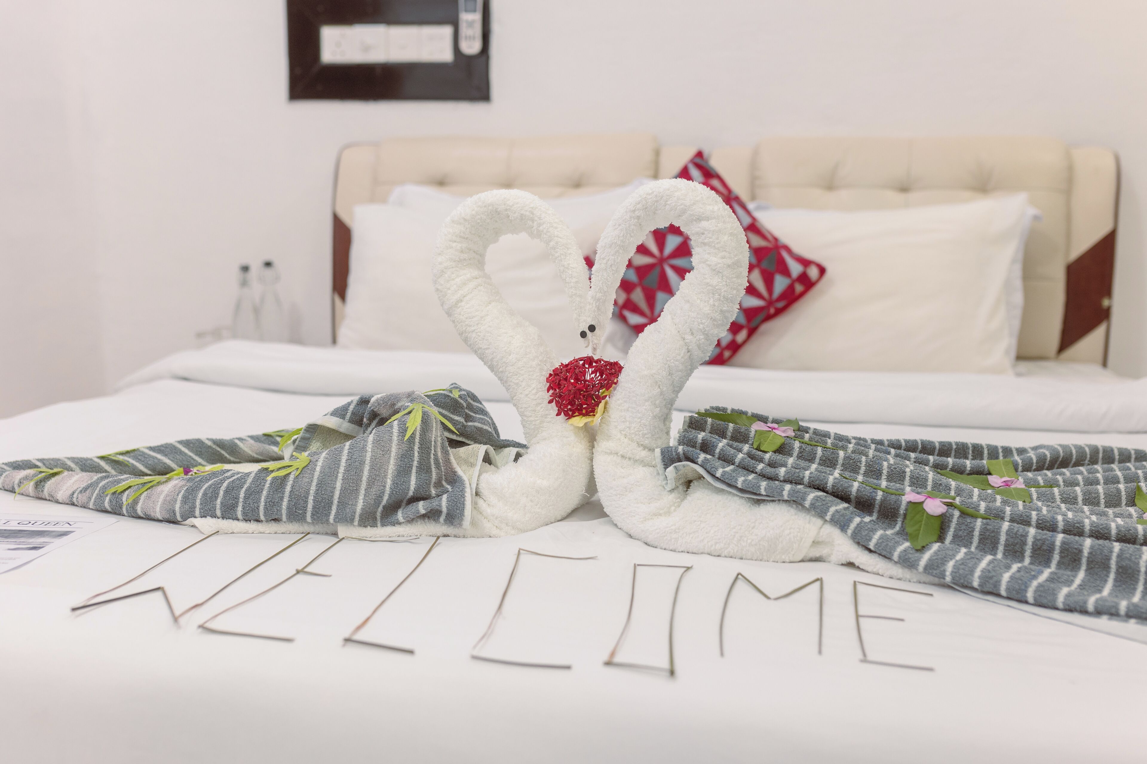 Een net opgemaakt bed met een handdoekje in de vorm van een hart en de tekst 'WELCOME' op het beddegoed.