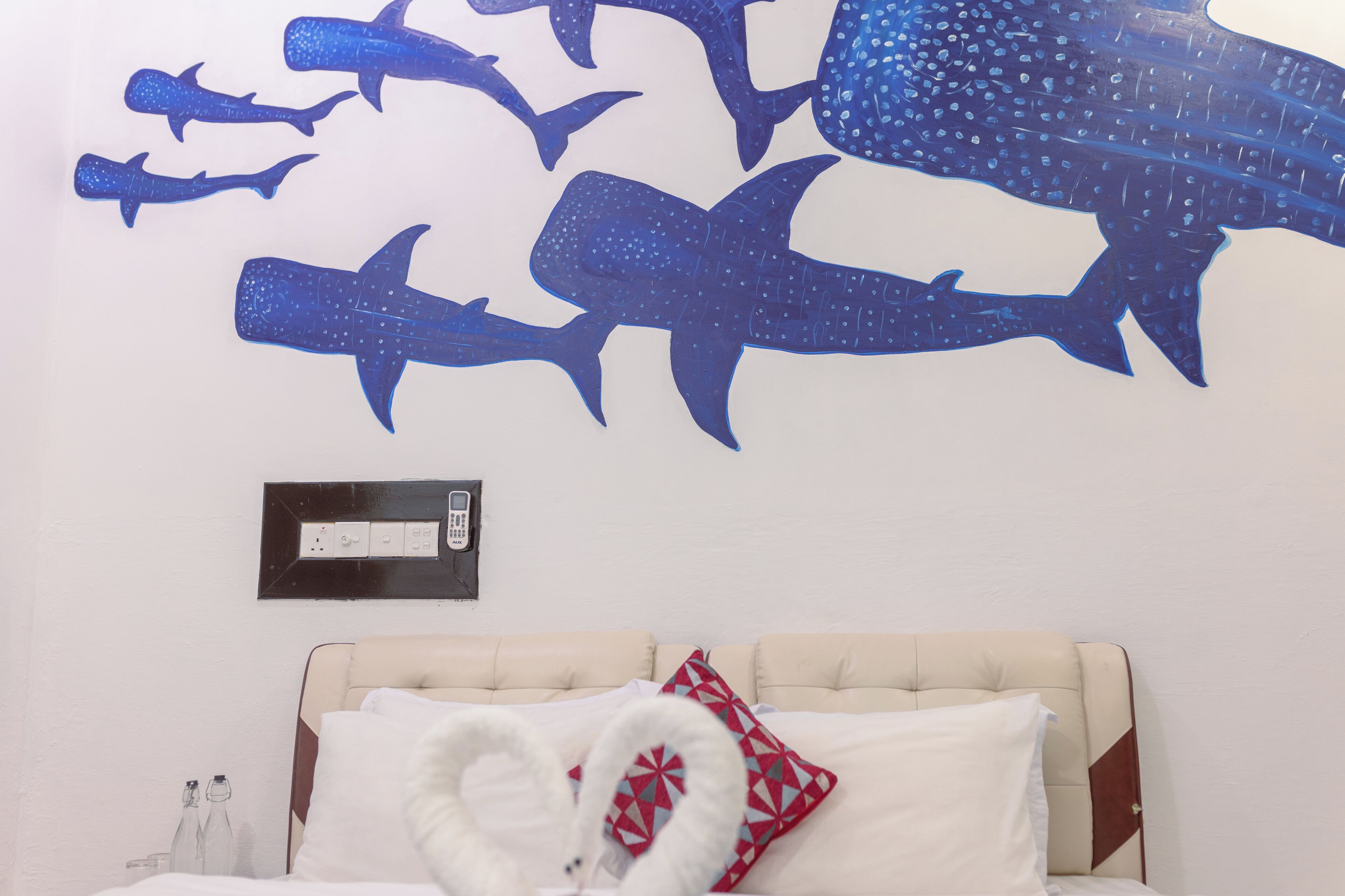 A hotel room with a bed, a wall-mounted light switch, and a wall decal of sharks.