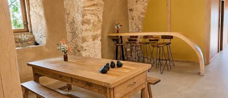 Un intérieur rustique avec une table et un banc en bois, des murs en pierre et un mur d’accent jaune.