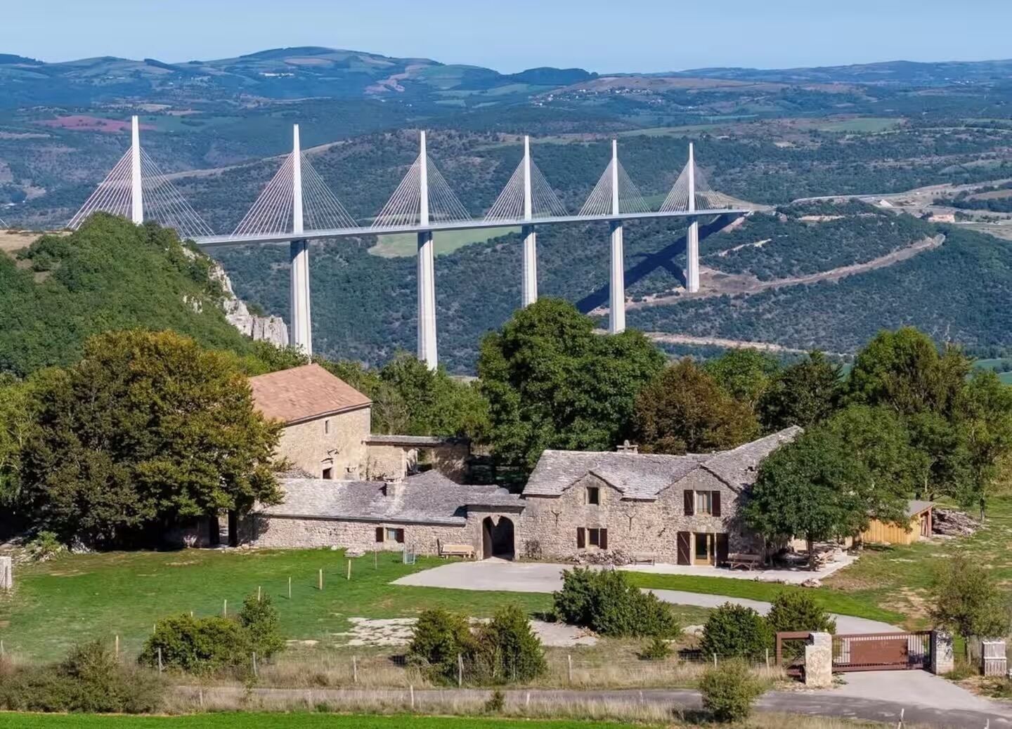 A stone building with a traditional design, surrounded by greenery and a view of a modern bridge.