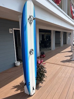 A surfboard leaning against a building with a potted plant nearby. - Cape May Harbor Getaway with Kayaks and Bikes (Cape May)