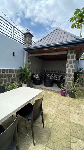 An outdoor patio with a stone wall, a metal roof, and potted plants. - Apartments - Furnished Condos - Yassa Douala - WILMA HOUSE: Just Like Home (Yassa)