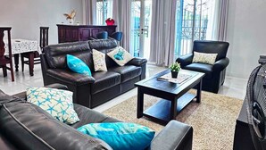 A modern living room with a black leather sofa, a coffee table, and a dining area with a table and chairs. - Apartments - Furnished Condos - Yassa Douala - WILMA HOUSE: Just Like Home (Yassa)