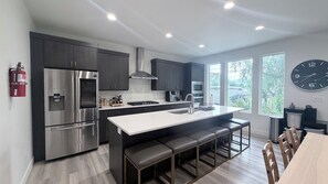 A modern kitchen with stainless steel appliances, a central island with bar stools, and a large window providing a view of the outdoors. - Ultimate 9BR/9BA Luxury Retreat @ SLC Central & Loaded (West Valley City)