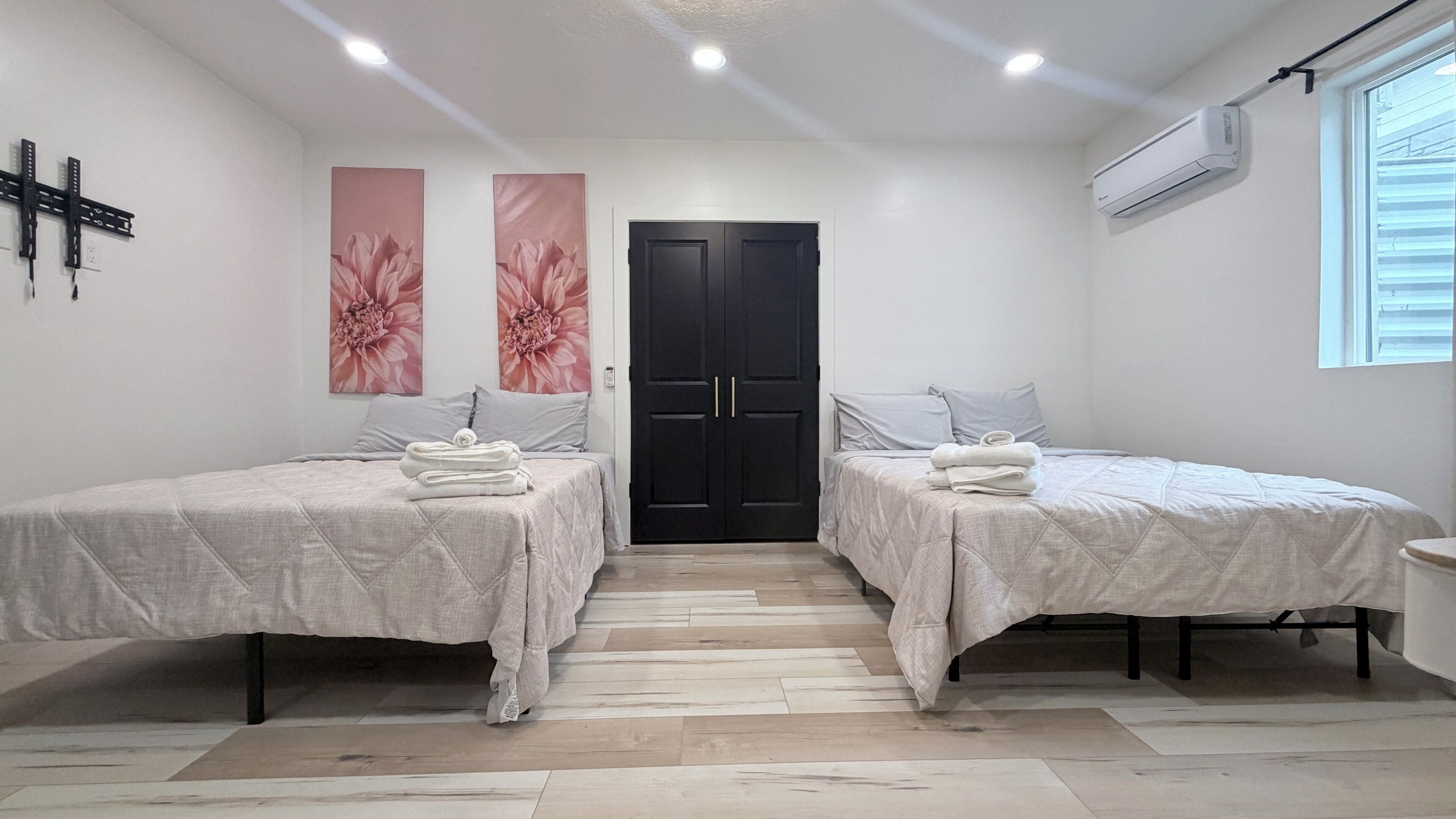 A hotel room with two beds, a black door, and a window with blinds.