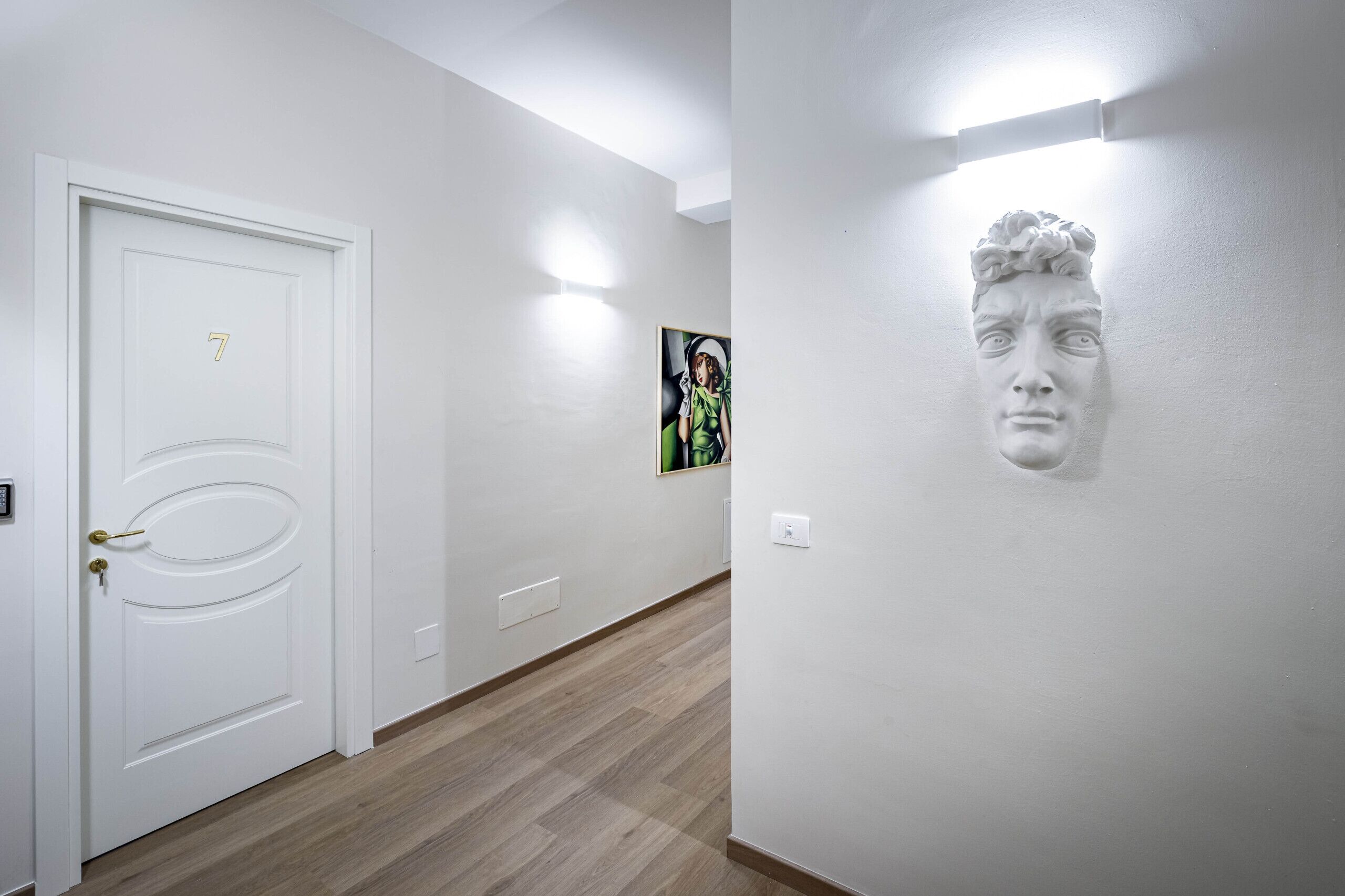 A hallway with a white door marked with the number 7, a light switch, and a wall-mounted light fixture.