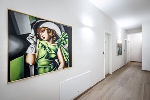 A hallway with a large painting on the left wall, a door on the right, and a wooden floor. - Seven Suites Central Apt 7 (Florence)