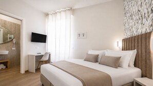 A hotel room with a bed, bedside tables, a desk, a chair, a television, and a bathroom with a mirror and towel rack.