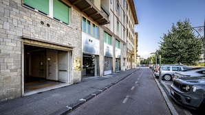 Vista de una calle con edificios en fila, algunos con persianas cerradas, y coches aparcados al lado.