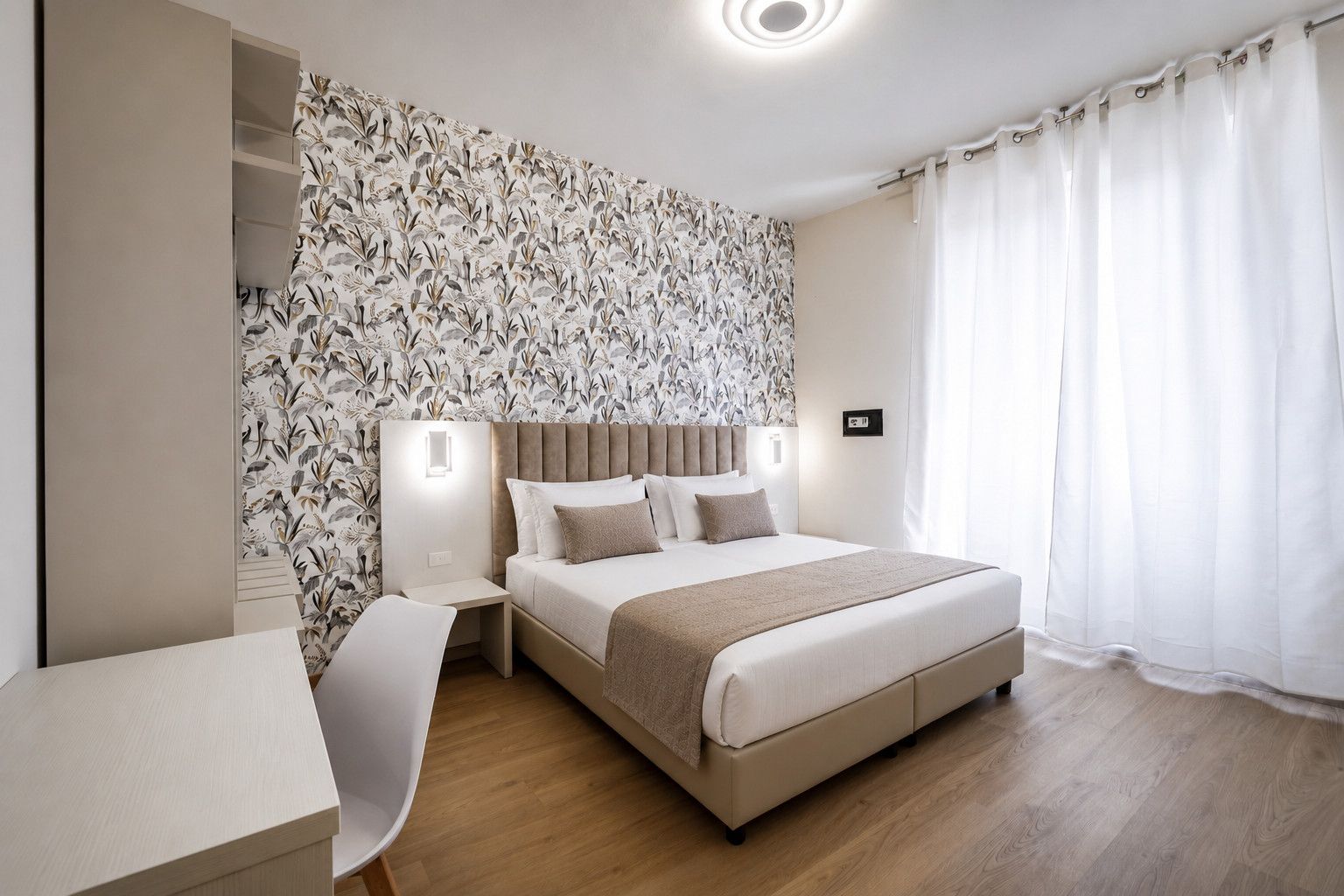 Een hotelkamer met een bed, nachtkastjes, een bureau en behang met een patroon.