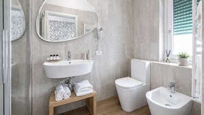 Un baño moderno con un lavamanos independiente, un inodoro, un bidé y un espejo con marco decorativo.