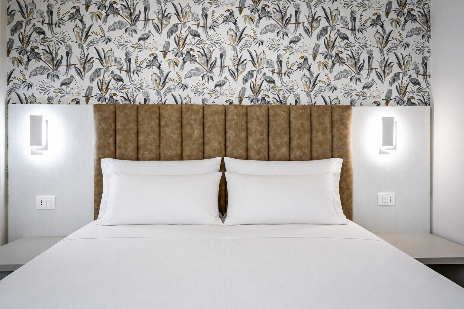 Una camera d'albergo con un letto, una testiera e una parete decorata con motivi floreali.