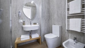 A modern bathroom with a white sink, round mirror, and a toilet.