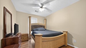 Une chambre à coucher avec un lit en bois, une télévision, une commode et un ventilateur de plafond.