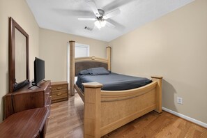 Ein Schlafzimmer mit einem Holzbett, einem Fernseher, einem Schminktisch und einem Deckenventilator.