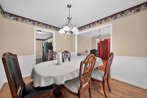 A dining room with a round table, six chairs, a chandelier, and a kitchen visible through an open doorway. - Quiet & Cozy 3BR Home w/ Soaking Tub + Laundry (Columbus)