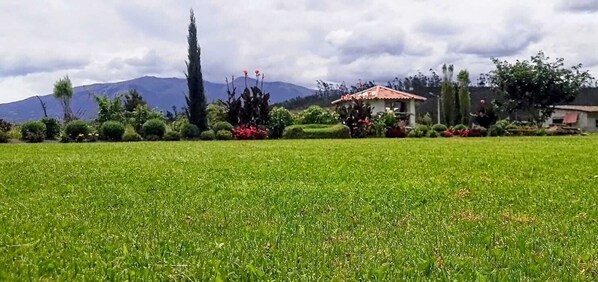 Un campo cubierto de hierba con un edificio de techo rojo y una montaña al fondo.