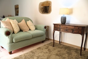 A room with a green patterned sofa, a wooden side table with a vase, and a beige carpet. - "casinha Das Portas" - A Medieval Village Retreat (Almeida)