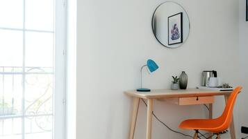 Une pièce avec un bureau en bois, une lampe de bureau bleue, une chaise orange, une petite plante en pot et un miroir rond accroché au mur.