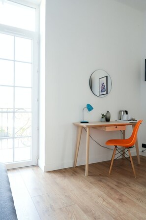 A room with a wooden desk, a blue desk lamp, an orange chair, a small potted plant, and a round mirror on the wall. - "Klein Blue®" room, a tribute to Yves Klein, which will bring out the best in ultramarine blue (NIMES)
