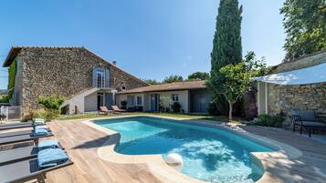 Un bâtiment en pierre doté d’une piscine, de chaises longues et d’une pergola.
