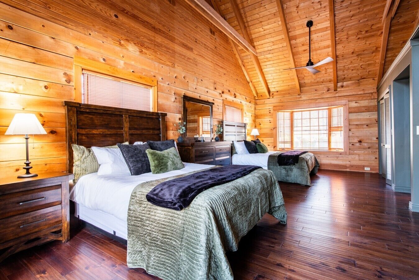 A log cabin bedroom with two beds, wooden floors, and a large window.