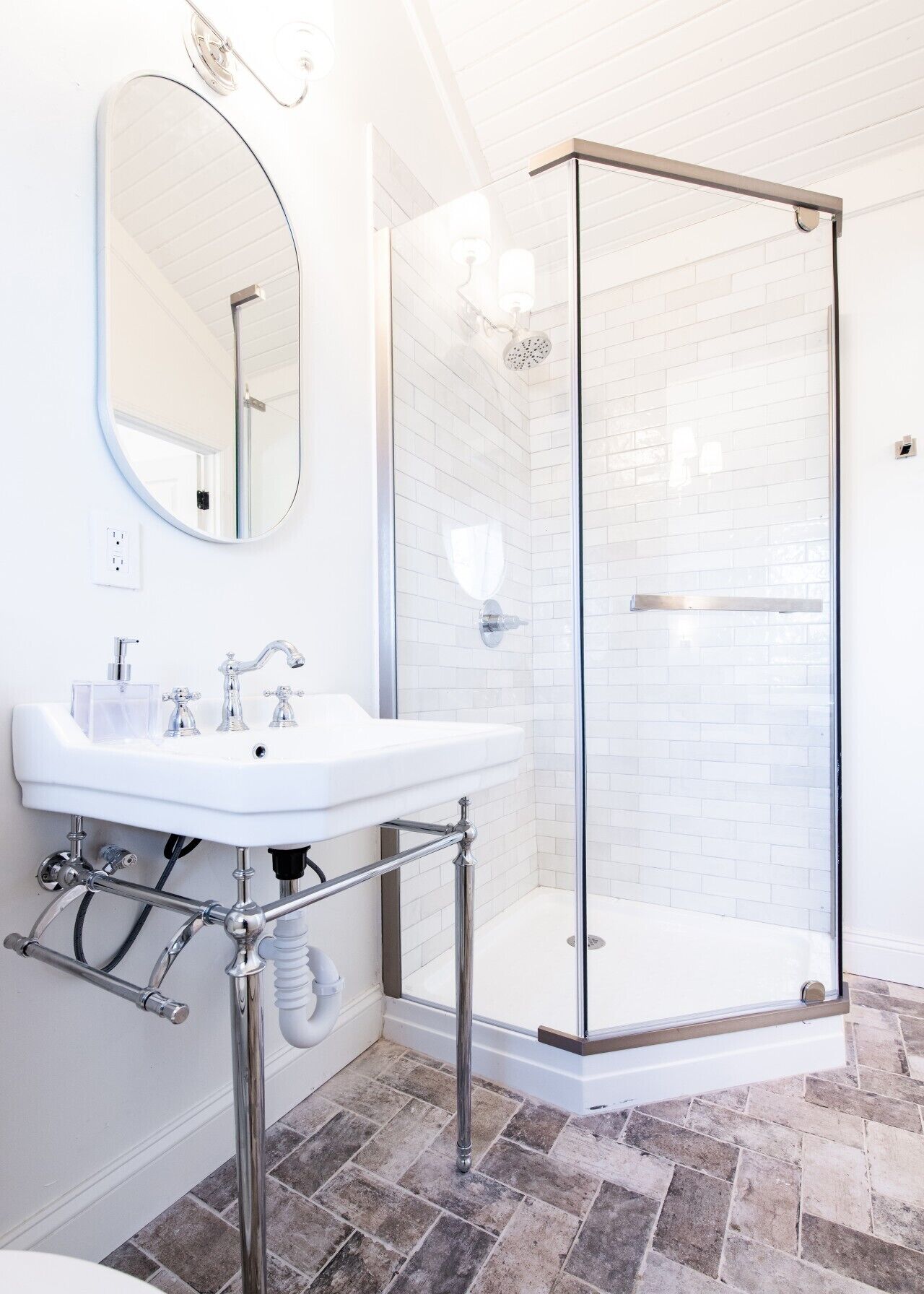 A bathroom with a white sink, a round mirror, and a glass-enclosed shower.