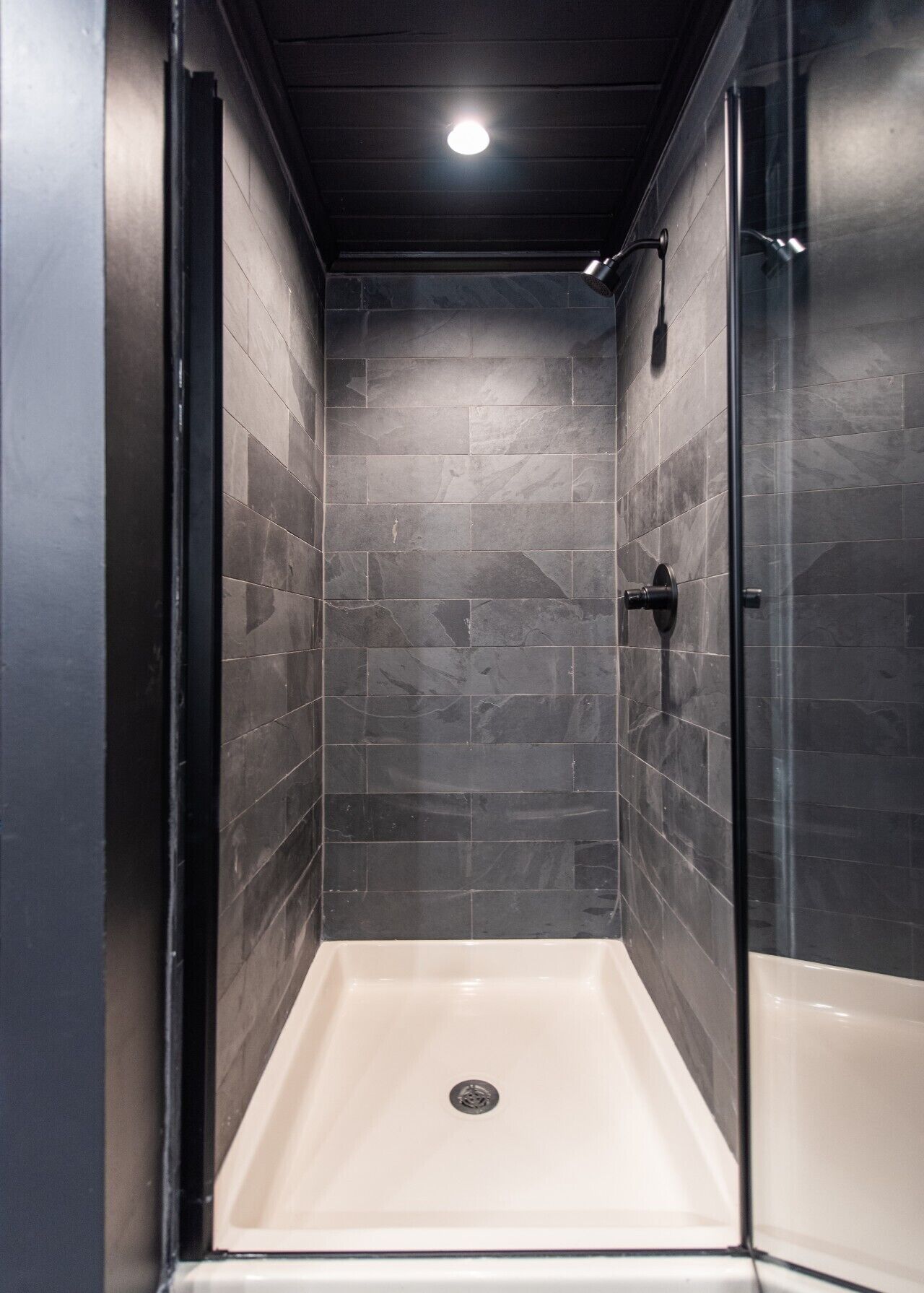 A walk-in shower with dark tiled walls and a glass door.