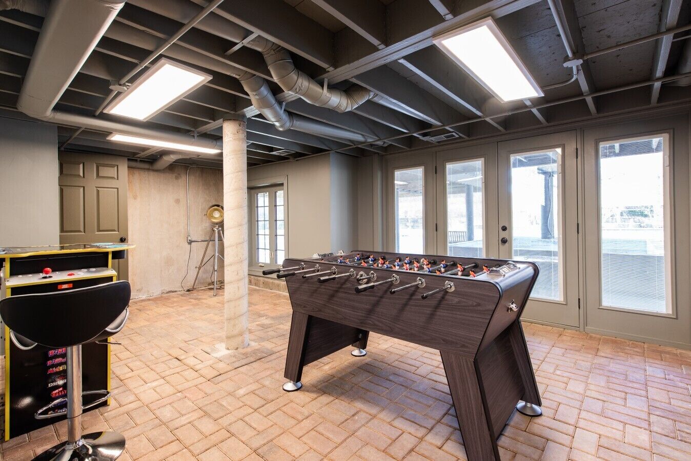 A room with a foosball table, a pool table, and a bar area with stools.